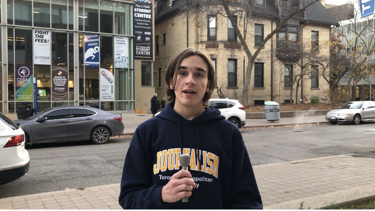 Mitchell Fox in the middle of reporter-on-camera segment, wearing a TMU journalism hoodie and a microphone