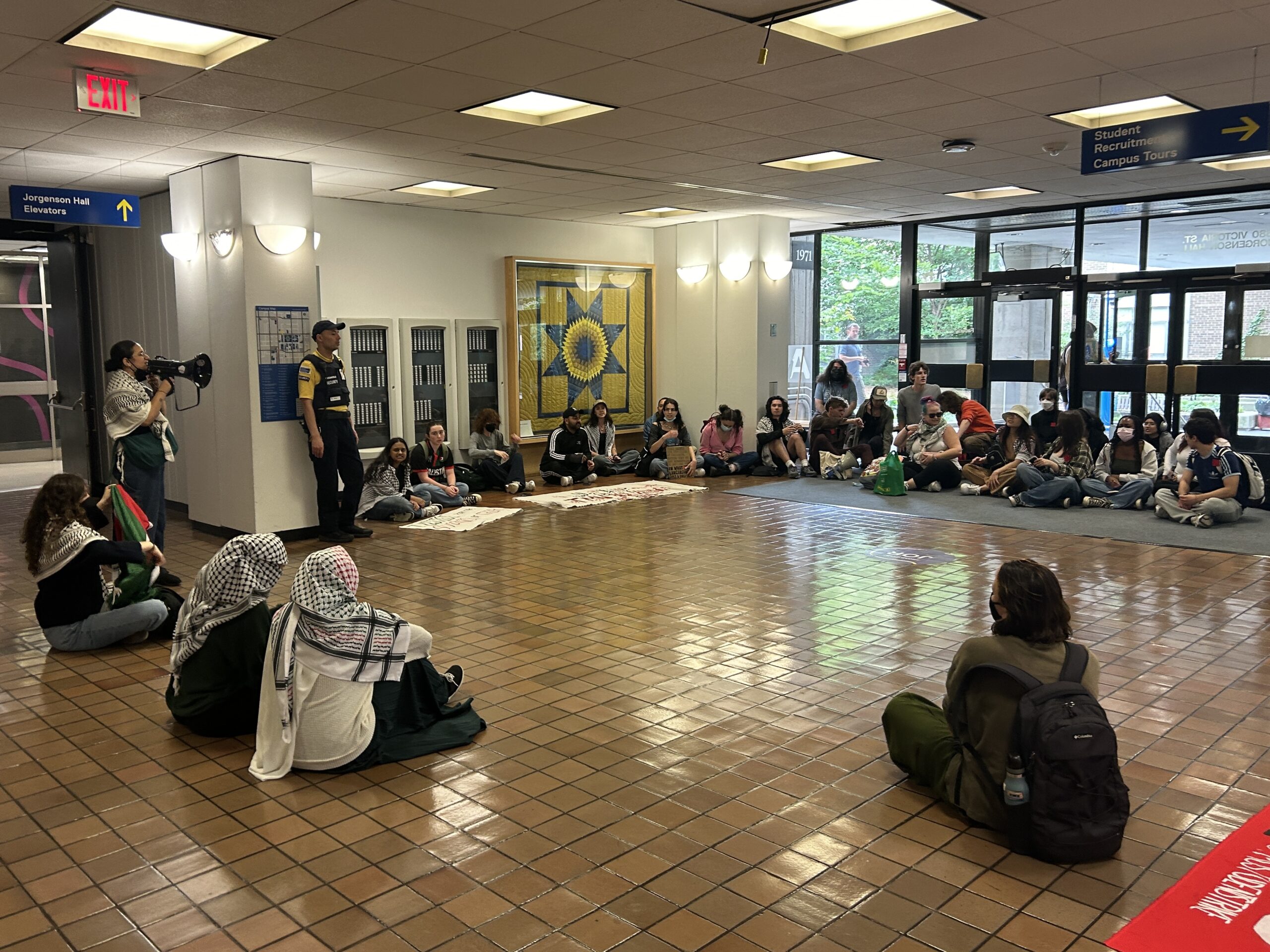 Students and staff sit in a circle near the entrance to a building at TMU. Many wear keffiyehs